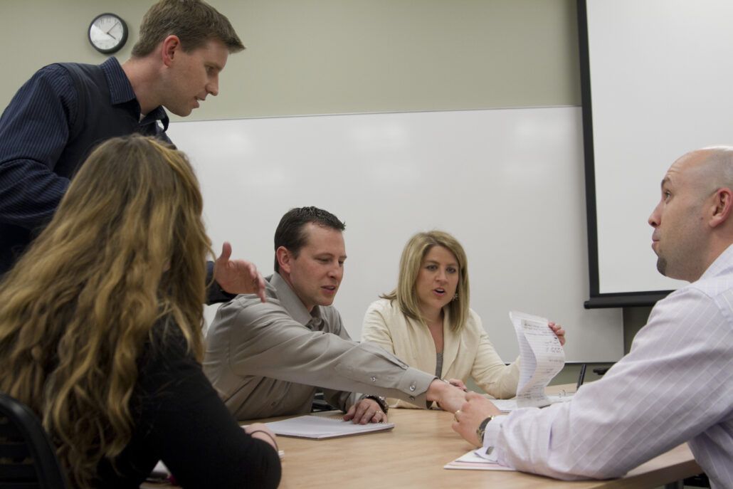 Five people sit around a table in a meeting room with papers in front of them.